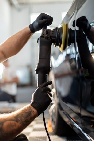 Professional man polishing black car and removing scratches in detailing center